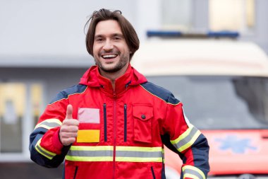 Laughing paramedic showing thumb up on street clipart