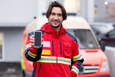 Boş ekran ile akıllı telefon tutarak kırmızı üniformalı gülümseyen sağlık görevlisi