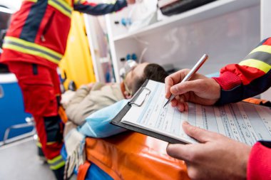 Partial view of paramedic writing diagnosis in clipboard clipart