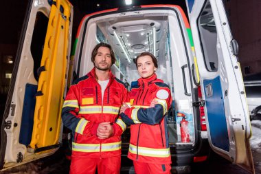 Paramedics in red uniform standing in front of ambulance car clipart