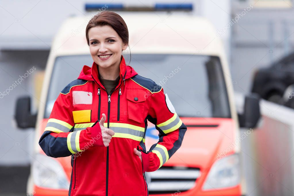 Charming female paramedic in red uniform showing thumb up