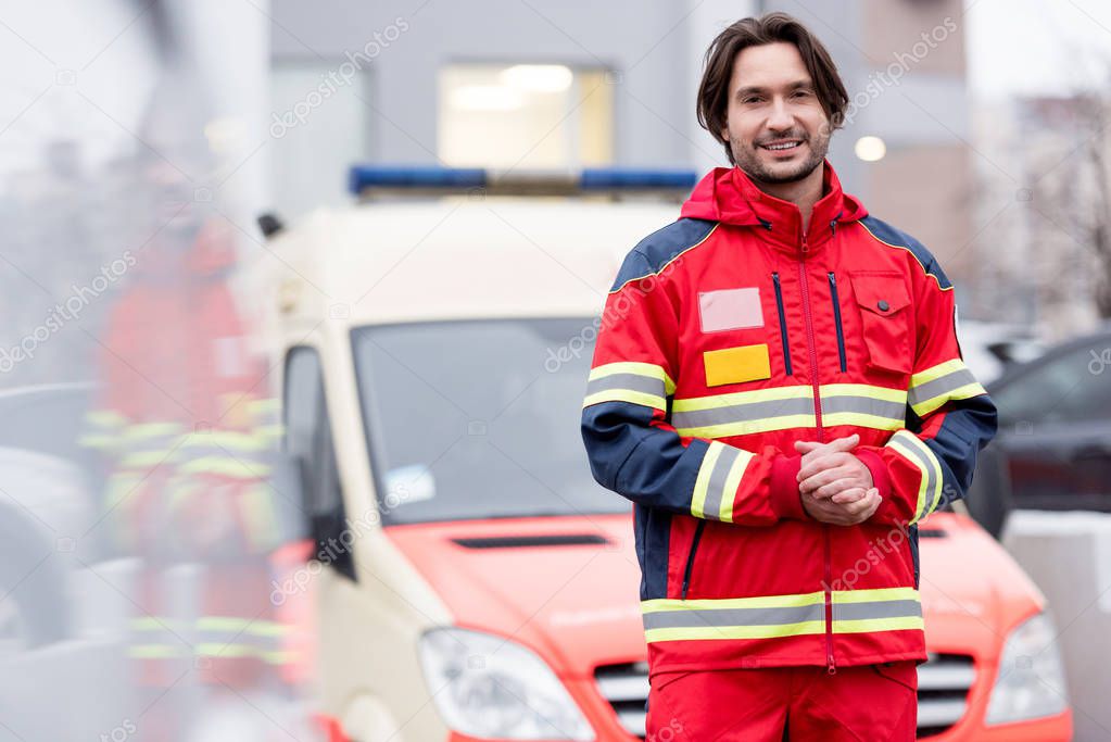 Smiling paramedic in uniform standing near ambulance car