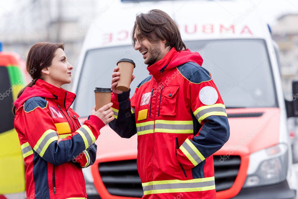 Smiling paramedics drinking coffee in front of ambulance car