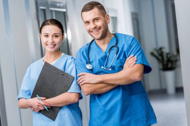 Smiling doctors in blue uniform holding stethoscope and clipboard clipart