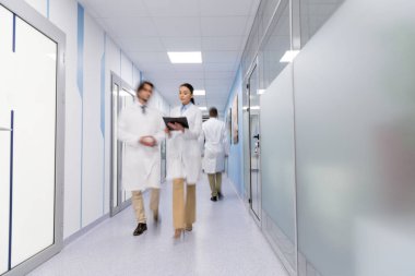 Doctors in white coats with black folder walking down hall clipart
