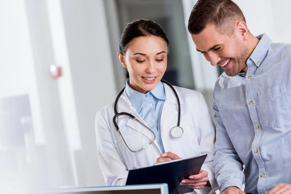 Médico Sonriente Hablando Con Paciente Escribiendo Portapapeles — Foto de Stock