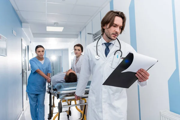 Médico Leitura Notas Enquanto Colegas Transportando Paciente — Fotografia de Stock