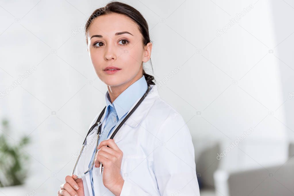 Pensive female doctor in white coat with stethoscope looking away