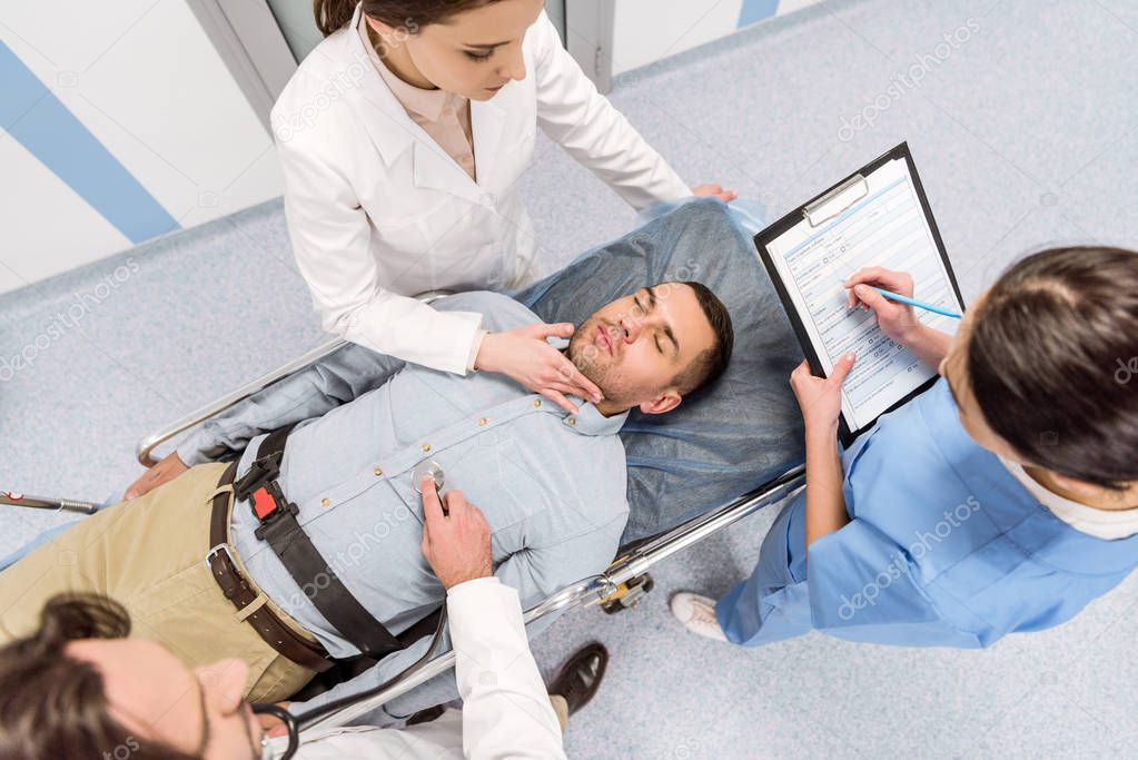 Top view of doctors transporting unconscious patient and checking pulse