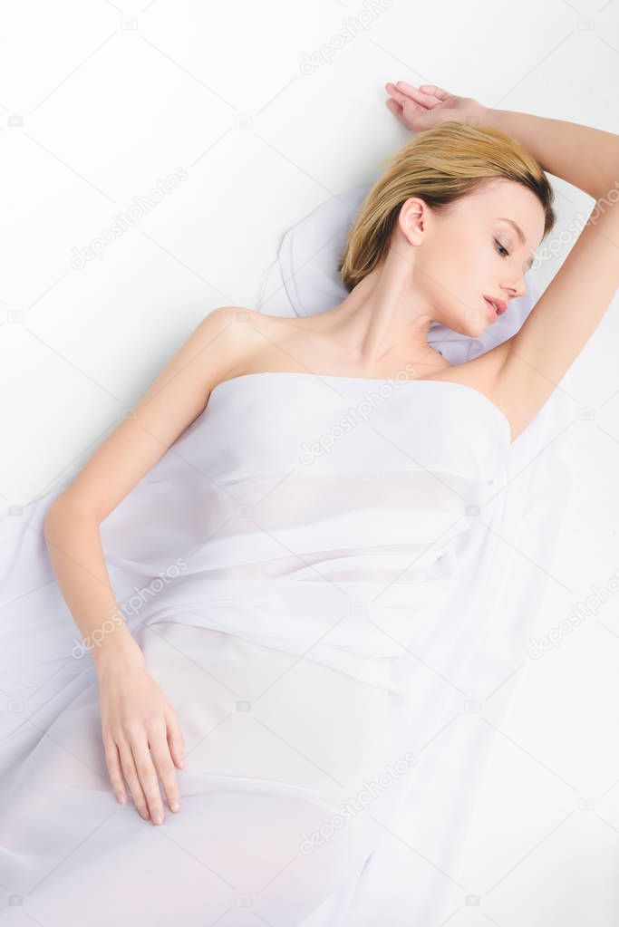 top view of elegant young woman with closed eyes lying in white cloth, isolated on grey
