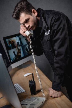 guard in uniform talking on telephone and looking at computer monitor  clipart