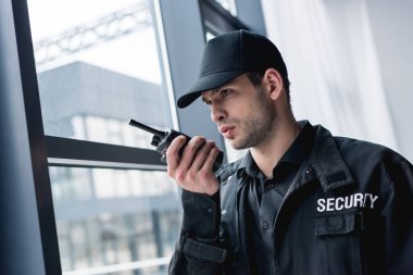 cropped view of guard in uniform talking on walkie-talkie and looking away clipart