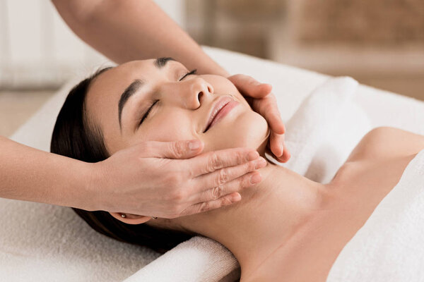  woman getting face massage with closed eyes at spa 