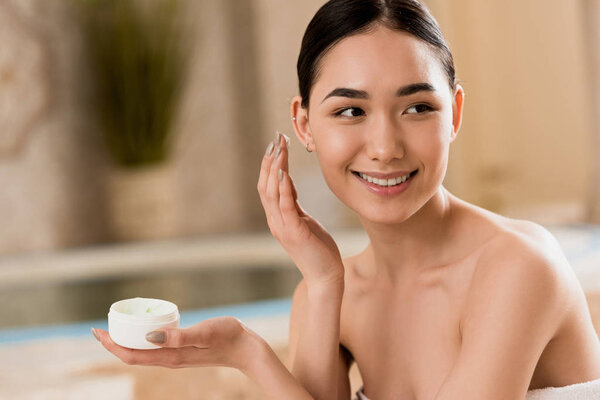 attractive asian woman applying cosmetic cream at spa with copy space 