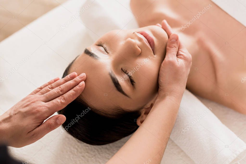attractive asian woman getting face massage with closed eyes at spa 