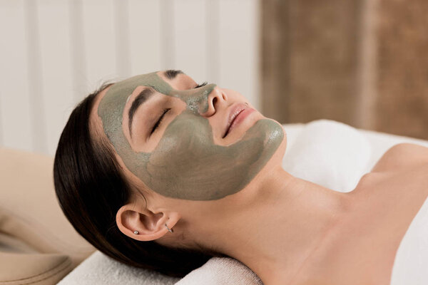 attractive asian woman lying with clay mask on face at spa 