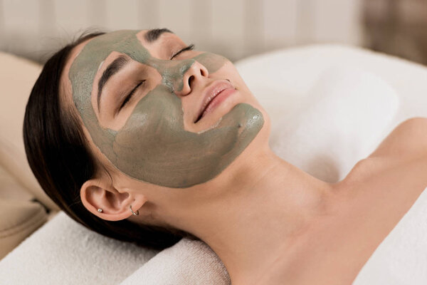 attractive asian woman lying with clay mask on face at spa 