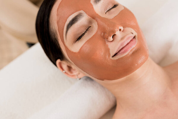 beautiful asian woman lying with clay mask on face at spa 