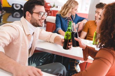 selective focus of smiling friends talking and cheering with soda and beer at cafe  clipart