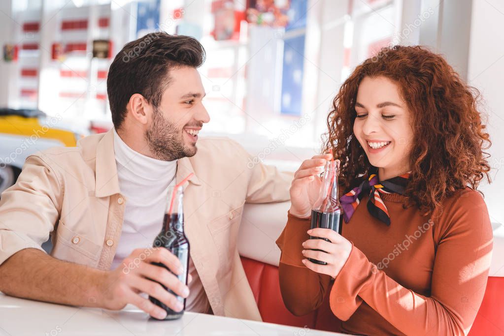  couple smiling and holding glass bottles with soda at cafe 