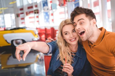 beautiful man and woman pointing with finger, smiling, hugging and looking away at cafe  clipart