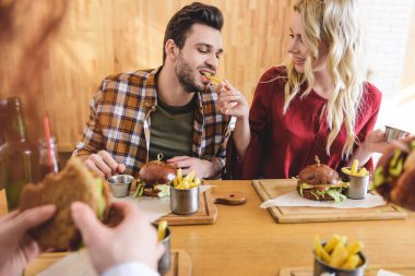 seçici odak kafede hamburger ve patates kızartması yiyen yakışıklı ve güzel arkadaşlar 