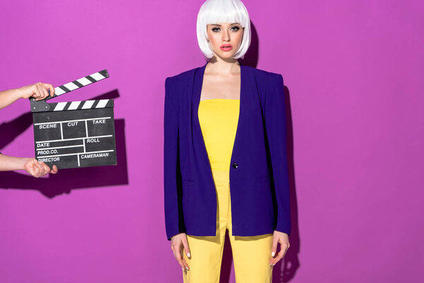 Confident girl in blue jacket and white wig standing on purple background