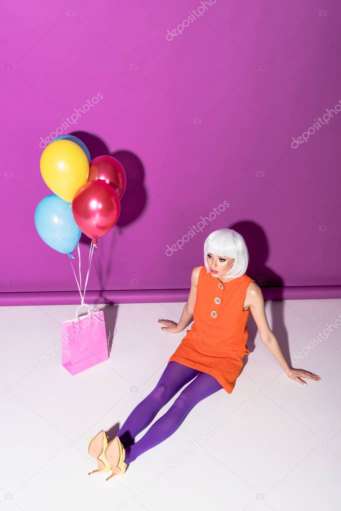 Gorgeous girl in white wig with air balloons sitting on purple background