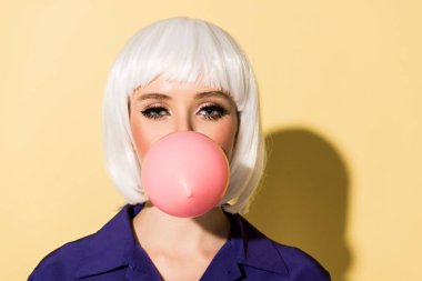 Attractive young woman in wig chewing bubble gum on yellow background clipart