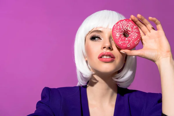 在紫色查出的美丽的年轻妇女在白色假发拿着甜甜圈 — 图库照片