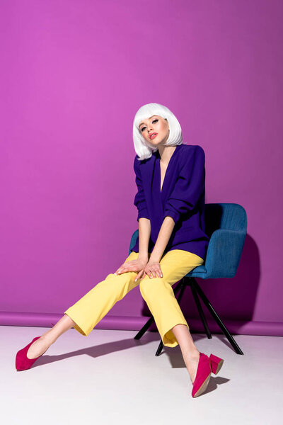 Attractive girl in white wig sitting in armchair on purple background