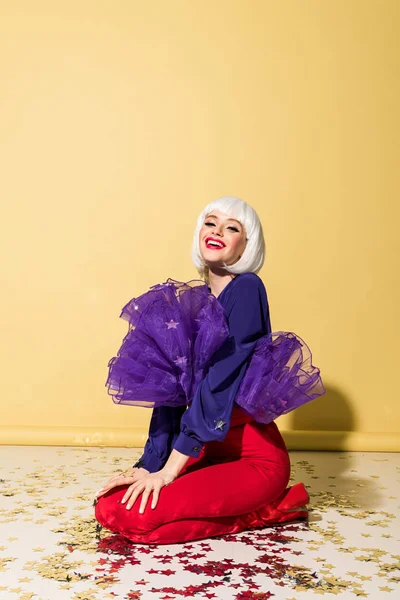 Sonriente Chica Impresionante Peluca Sentado Confeti Sobre Fondo Amarillo — Foto de Stock