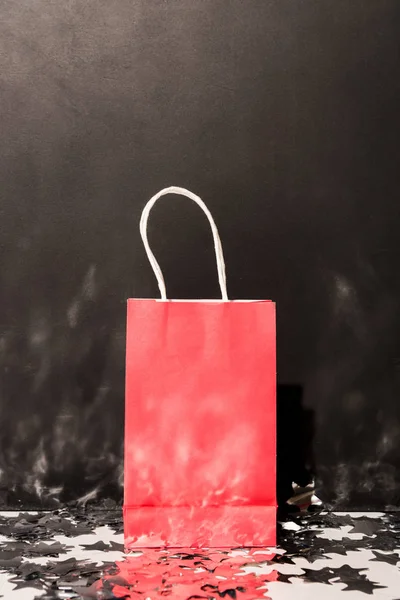 Red shopping bag standing on sparkle confetti on black background