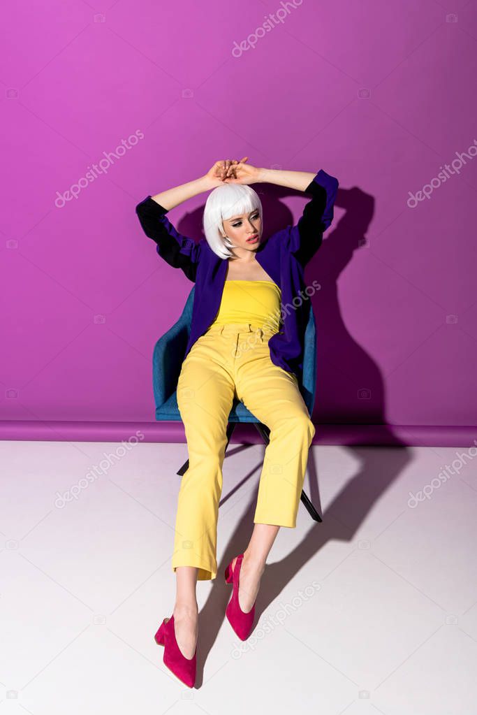Gorgeous young woman in white wig posing in armchair on purple background