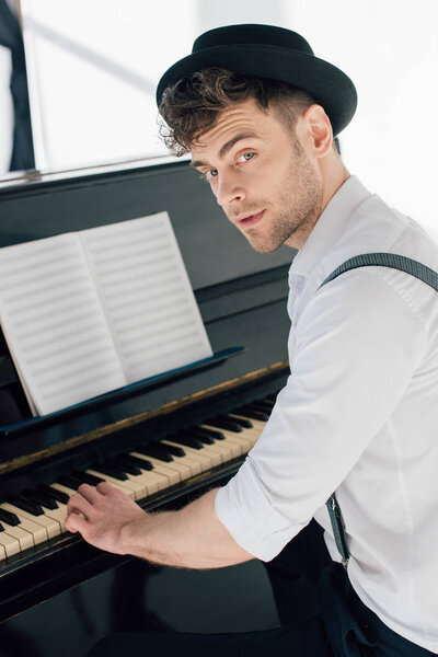 handsome pianist in stylish clothing playing piano at home