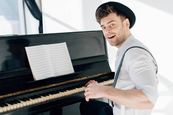 smiling pianist sitting by piano and looking at camera