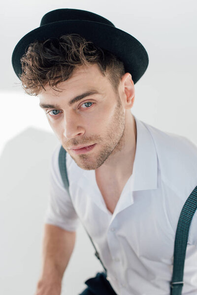 selective focus of handsome dreamy man in white shirt and black hat 