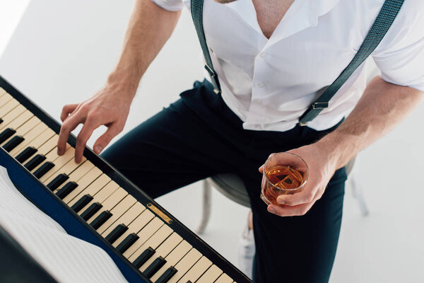 обрезанный вид пианиста, держащего стакан алкогольного напитка во время игры на фортепиано
 