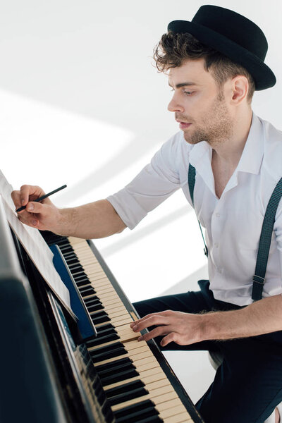 handsome composer writing in music book while sitting at piano 