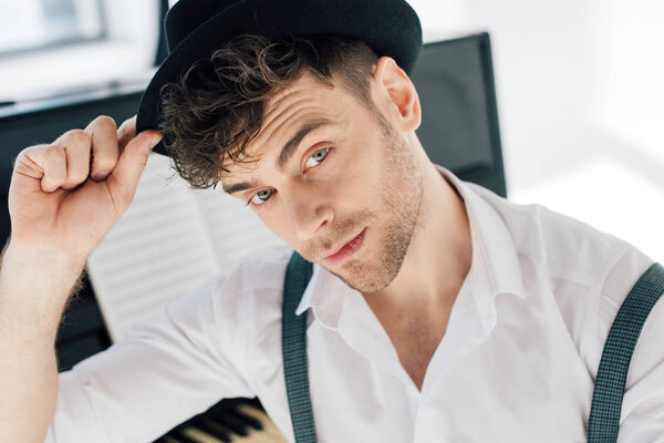 selective focus of handsome musician correcting hat and looking at camera