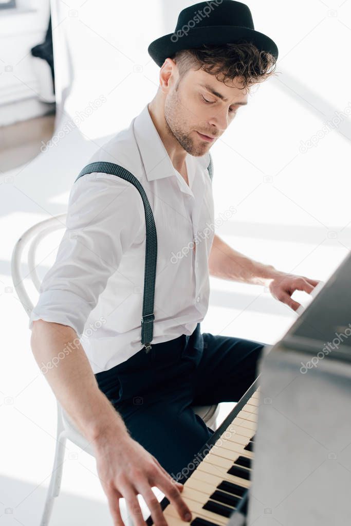 handsome pianist in white shirt and black hat playing piano 