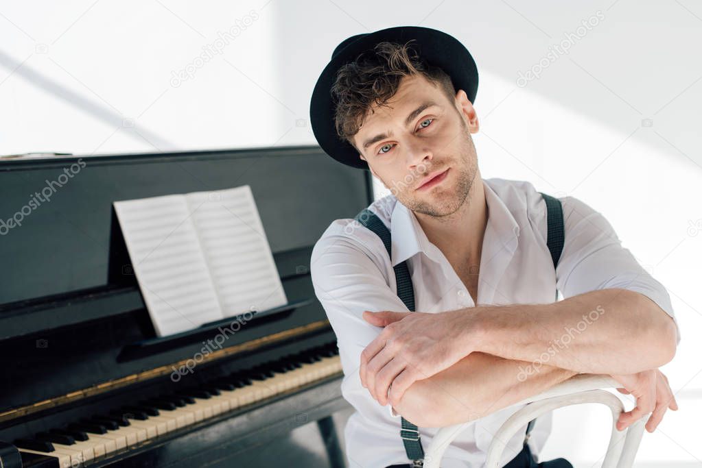 dreamy pianist in white shirt and black hat looking at camera