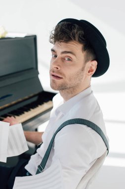 selective focus of handsome musician sitting by piano and looking at camera  clipart