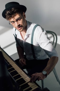 smiling musician in spectacles playing piano and looking at camera  clipart