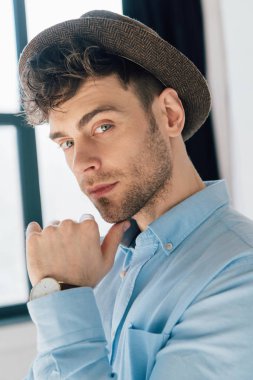 mavi gömlek ve kahverengi şapka ayakta evde pencere tarafından yakışıklı adam portresi