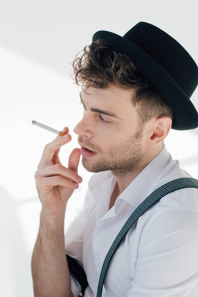 handsome man in white shirt and black hat smoking cigarette