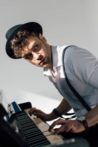 selective focus of serious musician in black hat playing piano 