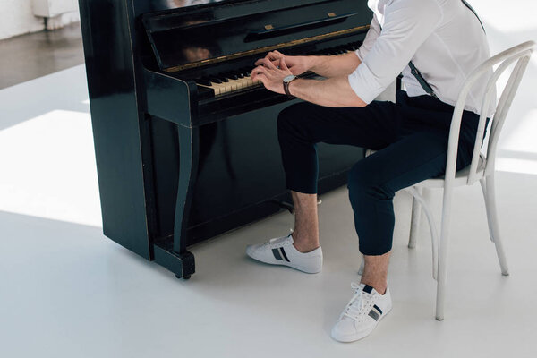 partial view of musician in sneakers playing piano at home