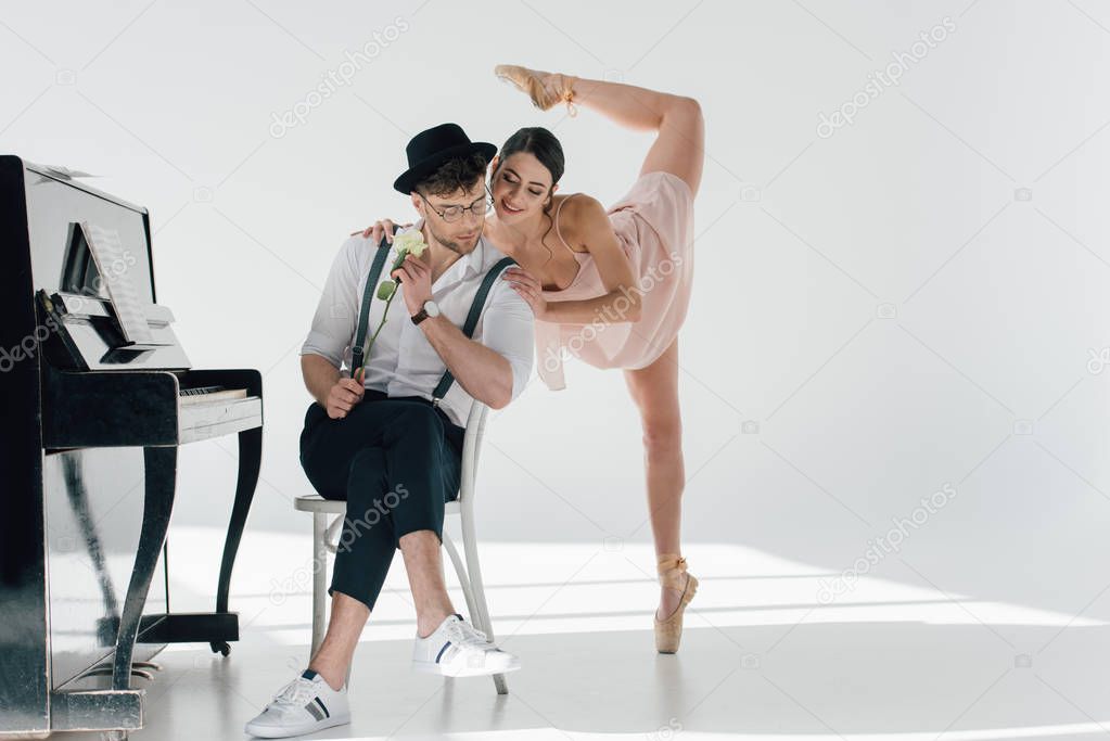 handsome musician sitting on chair with rose while young ballerina dancing near him 