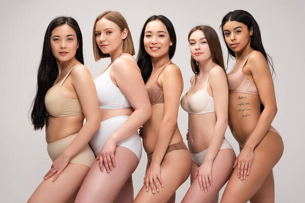 five attractive multicultural girls in underwear posing at camera and smiling isolated on grey, body positivity concept 